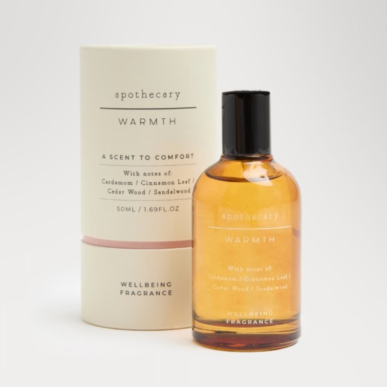 Amber-colored bottle labeled "apothecary WARMTH" with matching cylindrical box. Text notes scents of cardamom, cinnamon leaf, cedar wood, and sandalwood. 50ml size.
