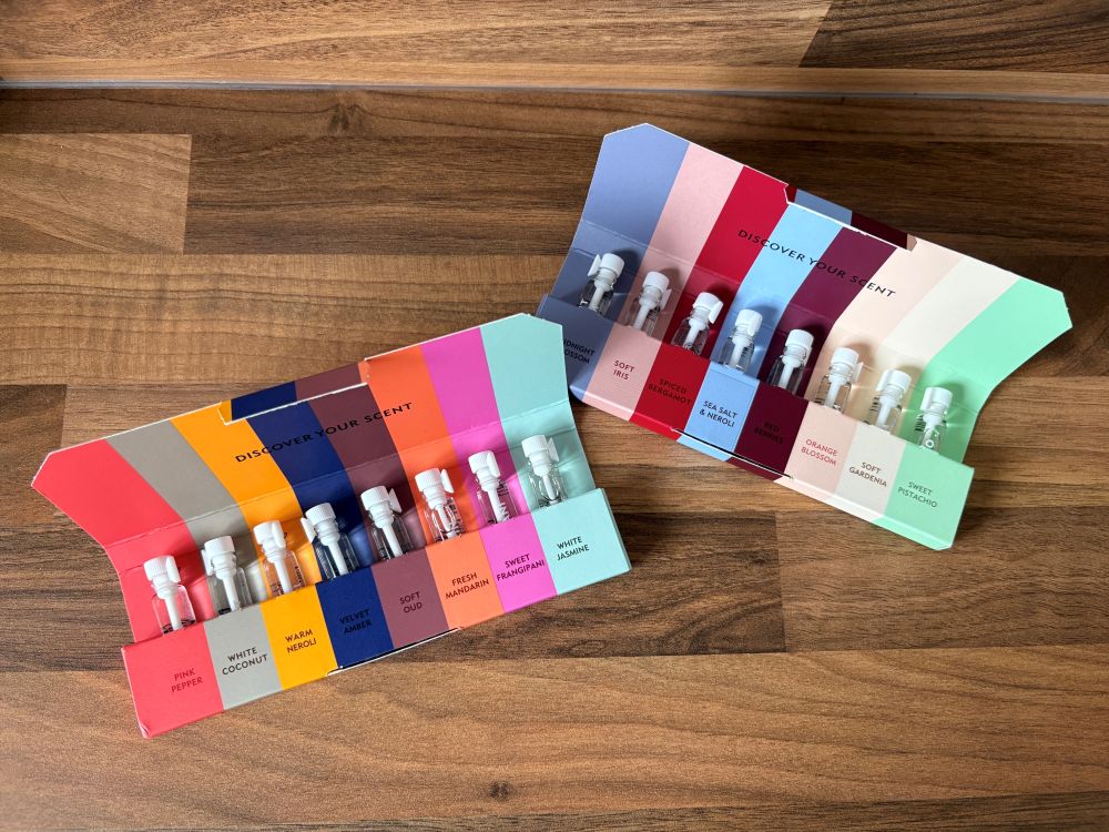Two open sample fragrance sets with colorful packaging, each containing five small glass vials of different perfumes, displayed on a wooden surface.