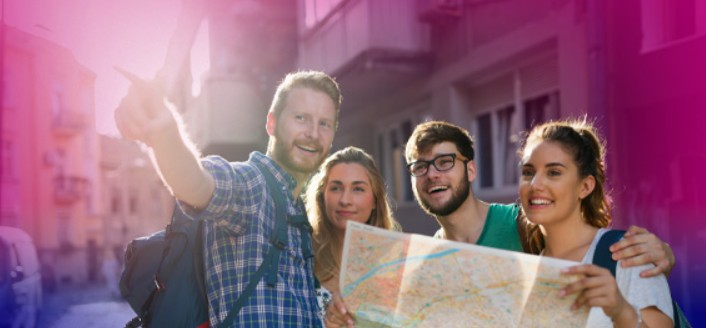 Four young adults stand together outdoors, looking at a map. One person points ahead, and they all appear to be smiling. The image has a pink and purple tint.