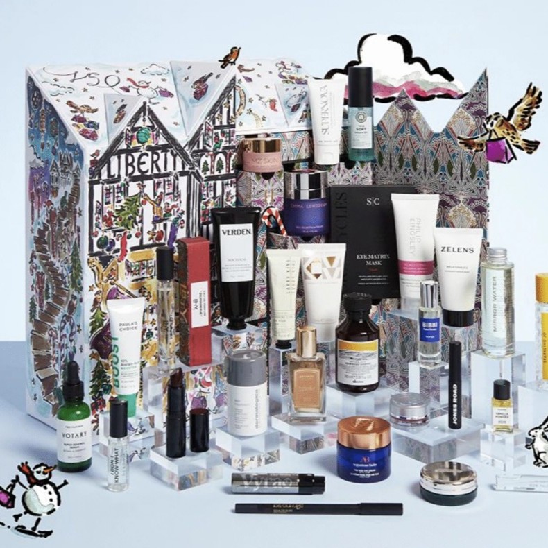 liberty beauty advent calendar 2026 A collection of various skincare, make-up, and beauty products displayed in front of a decorative, illustrated Liberty London advent calendar box.
