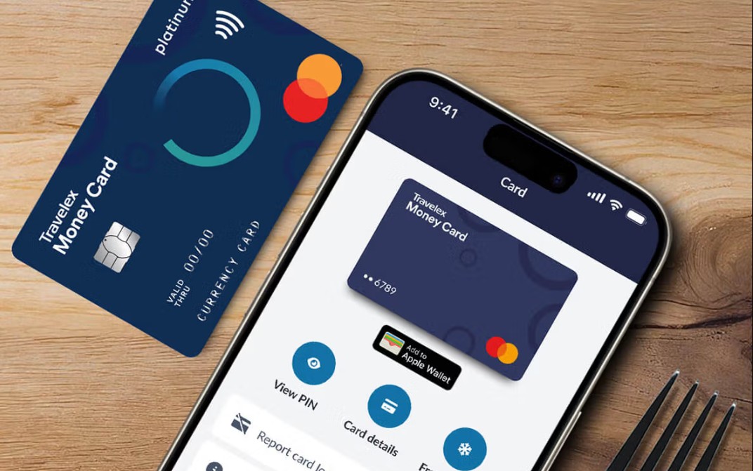 travelex desktop A Travelex Money Card beside a smartphone displaying the same card’s details in a digital wallet app on a wooden surface.