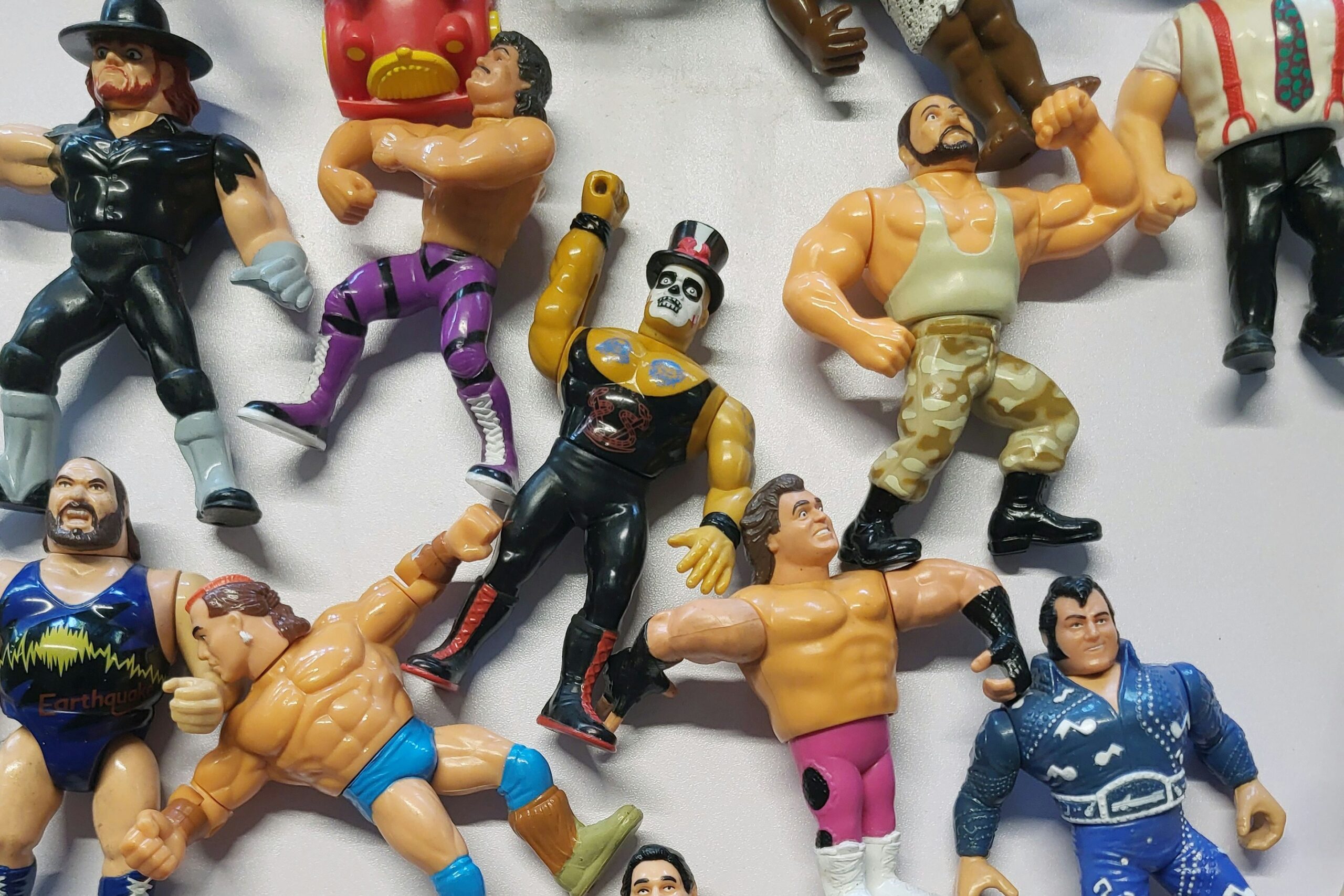 vintage toys A collection of vintage wrestling action figures arranged on a white surface, featuring various colorful costumes and poses.