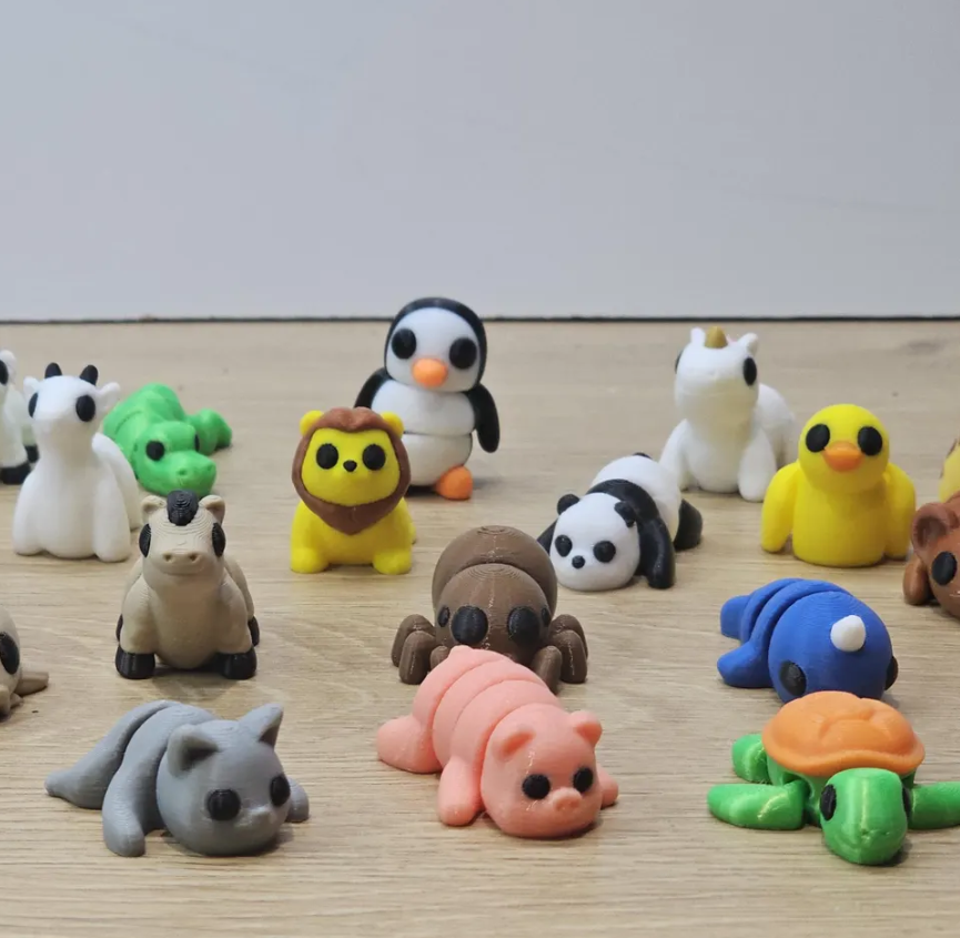 Assorted colourful animal figurines made from clay are arranged on a wooden surface against a plain background.