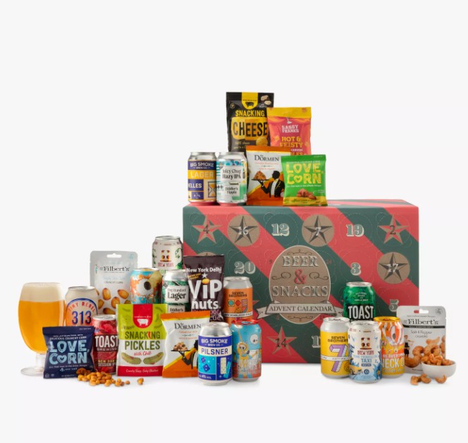 john lewis beer and snacks advent calendar 2026 A variety of beer cans and snack packets are displayed in front of a red and green advent calendar box, with a glass of beer and scattered nuts on the surface.