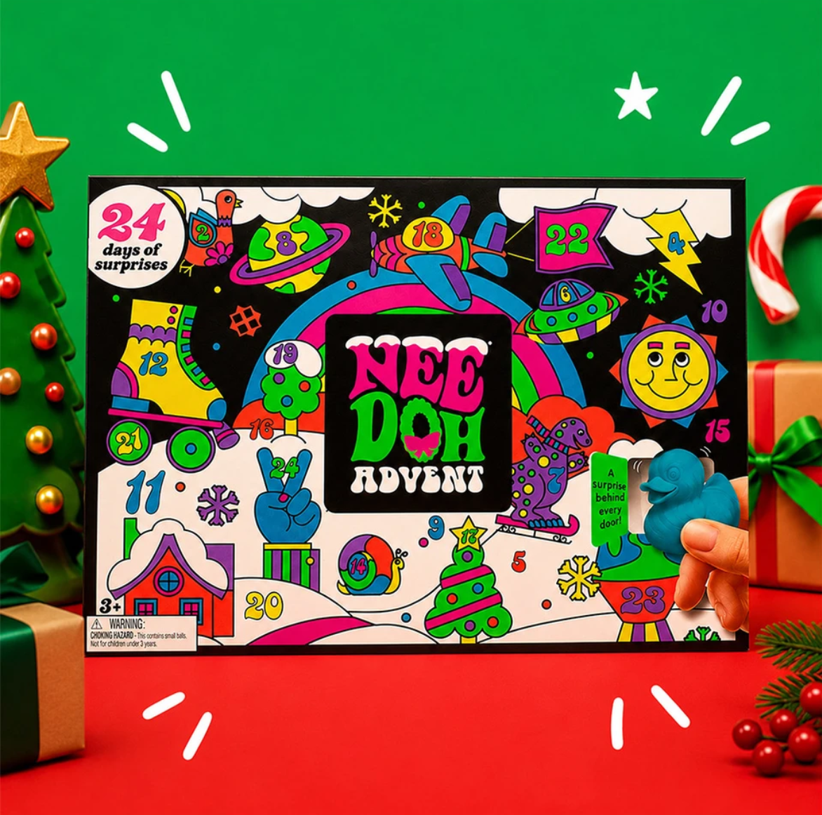 Colourful Nee Doh Advent calendar box with numbered doors, festive holiday drawings, and a hand opening a slot to reveal a blue toy. Christmas tree and decorations are in the background.