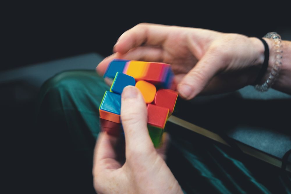 A person’s hands are manipulating a colourful, partially scrambled Rubik’s Cube against a dark background.