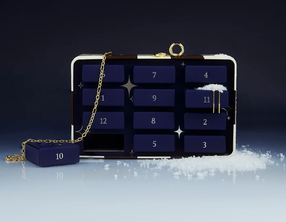 A navy blue box with numbered compartments, gold chain, and scattered white powder resembling snow sits against a dark gradient background.