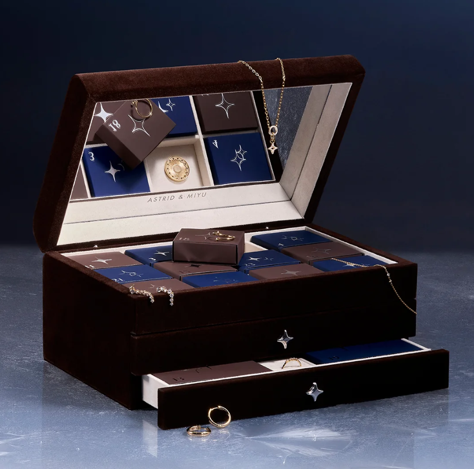 An open velvet jewellery box displays assorted rings, necklaces, earrings, and jewellery boxes neatly organised inside compartments and a drawer.