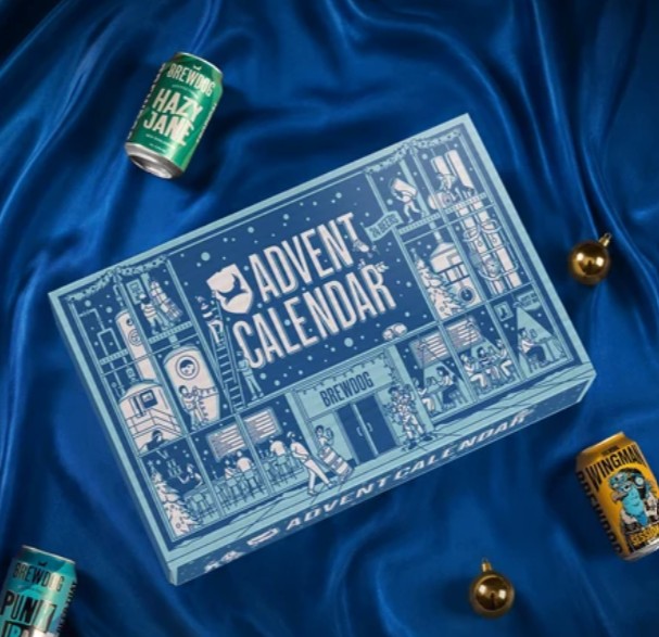 brewdog advent 2026 A BrewDog Advent Calendar box is on blue fabric, surrounded by three beer cans and two gold ornaments.