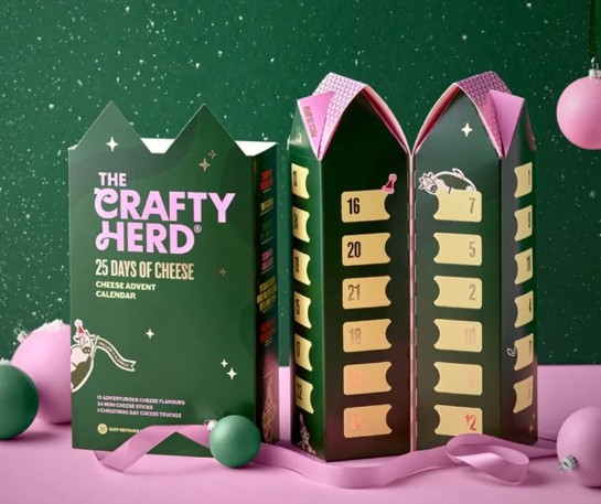 crafty-herd-cheese-advent A green cheese advent calendar box labelled “The Crafty Herd” stands open, revealing numbered doors. Pink baubles and a green backdrop complete the scene.