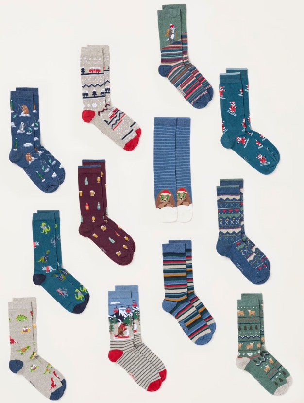 fatface men's Twelve pairs of colourful socks with various patterns, including stripes, holiday themes, animals, and geometric designs, are arranged on a white background.