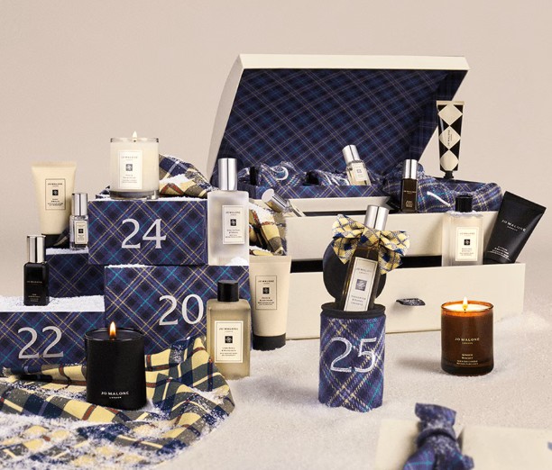jo malone advent calendar 2026 Display of Jo Malone products including candles, perfumes, creams, and gift boxes with numbers 20, 22, 24, and 25, arranged on a white surface with a checked pattern.