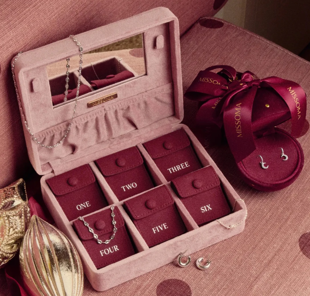 missoma silver advent calendar 2026 A pink jewellery box with six numbered compartments displays silver necklaces and earrings. Next to it is a round burgundy box with a ribbon, also holding a pair of silver earrings.