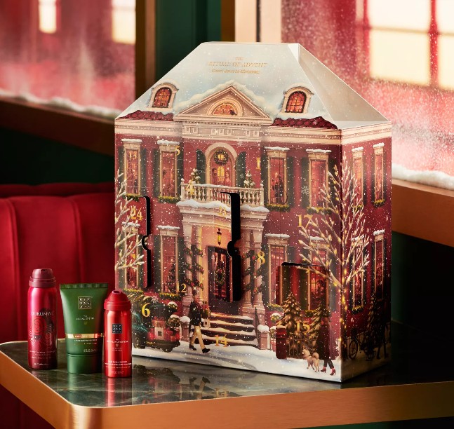 rituals advent calendar 2026 A holiday-themed advent calendar shaped like a house sits on a table, with three Rituals brand bath product bottles placed in front.