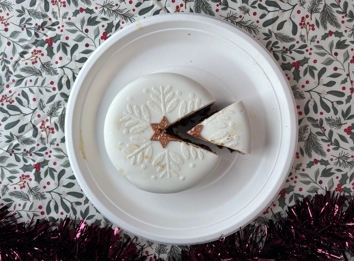 aldi christmas cake top-down A round white cake with an embossed snowflake pattern and a bronze star topper, with one slice removed, sitting on a white plate.