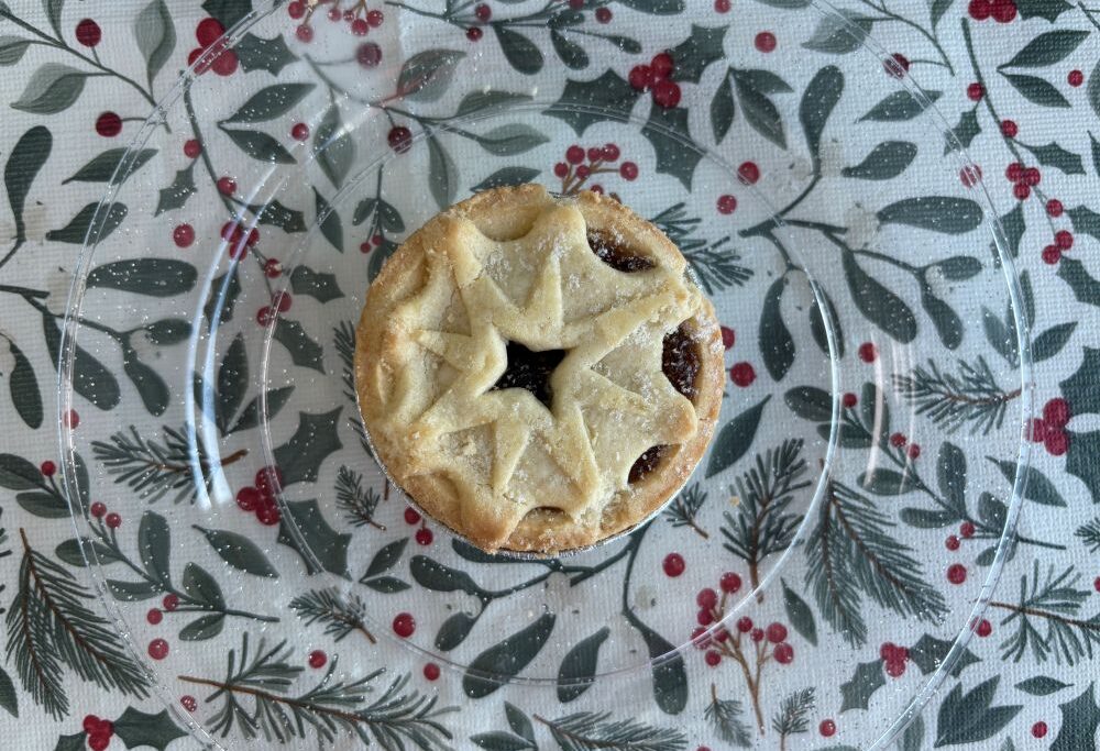 A single star-shaped mince pie on a clear plate over a holiday-themed tablecloth.
