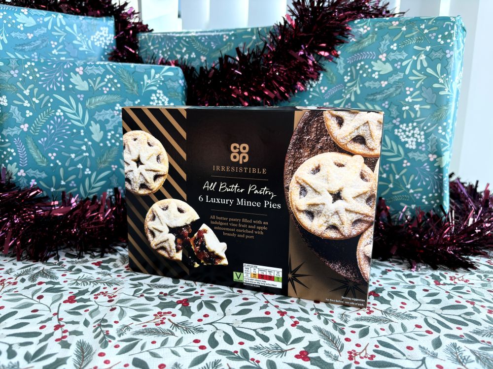Box of Co-op Irresistible All Butter 6 Luxury Mince Pies surrounded by festive gift wrap and tinsel.