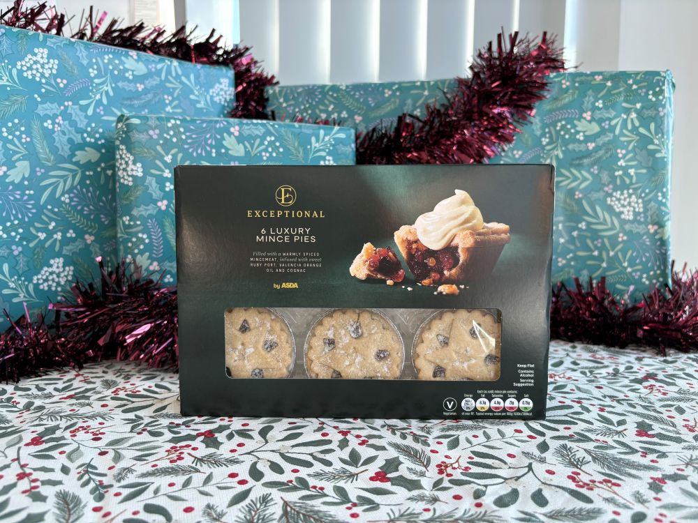 A box of six luxury mince pies by Asda, sitting in front of holiday-themed wrapped presents and tinsel.