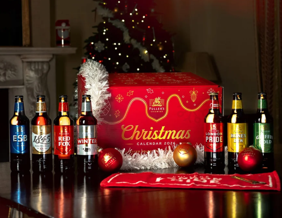 A red “Christmas Calendar 2023” beer box is surrounded by seven beer bottles, Christmas decorations, and a lit tree in the background.