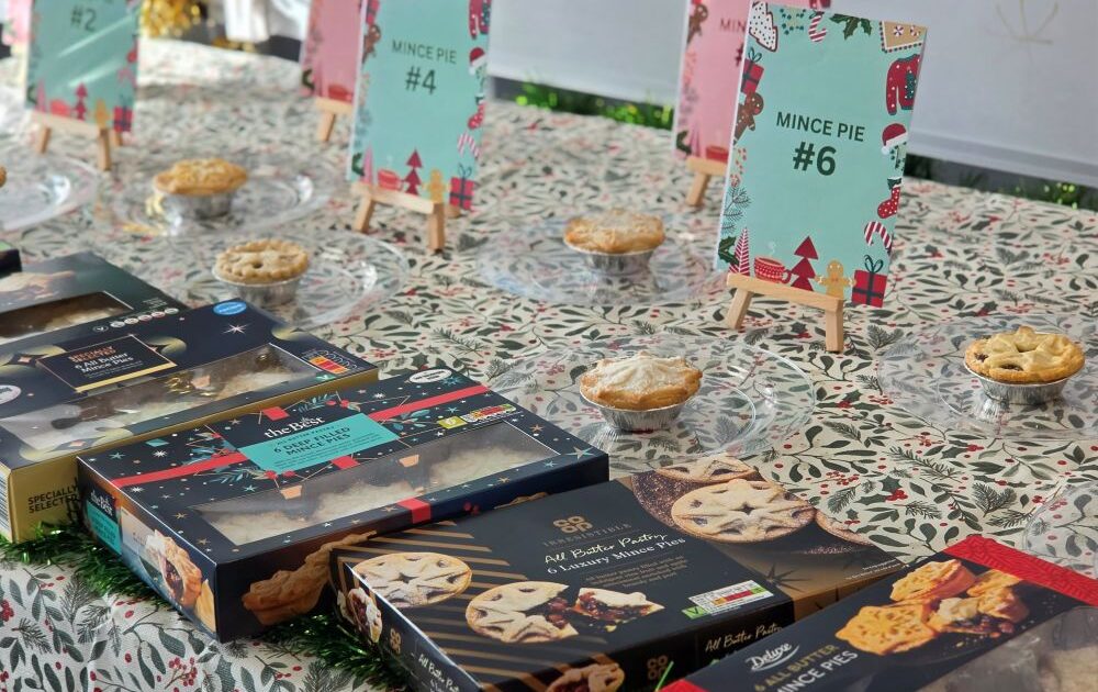 Boxes of mince pies and individual pies with numbered signs arranged on a tablecloth.